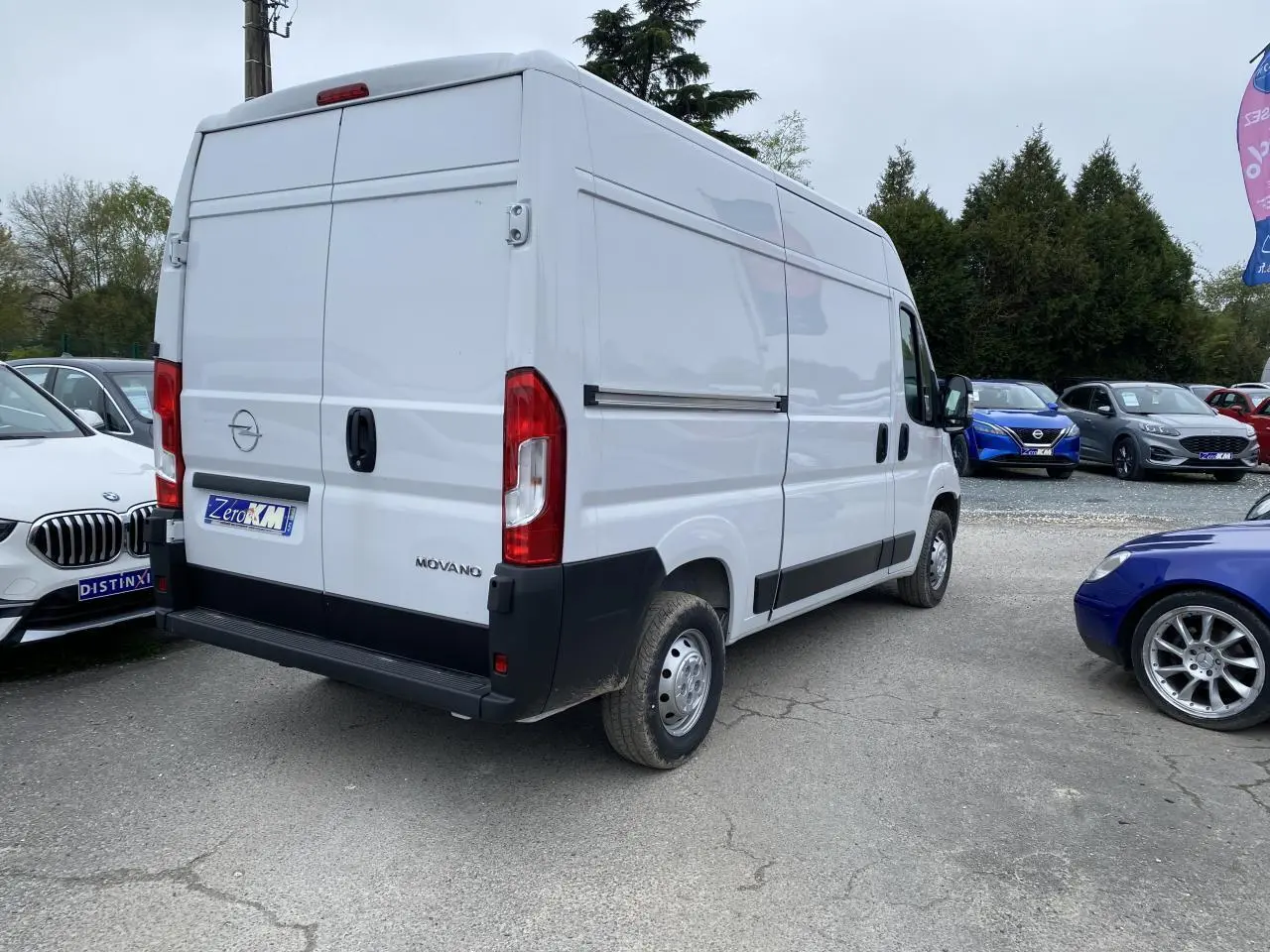 Vue 3/4 arrière droite d'un Opel Movano Fourgon blanc avec portes arrière fermées sur un parking.