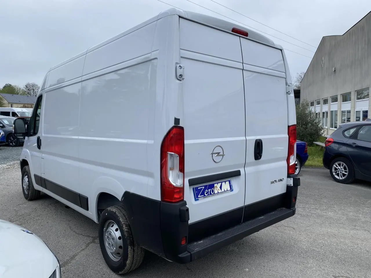 Vue 3/4 arrière droite d'un fourgon Opel Movano blanc avec portes arrière battantes et pare-chocs noir.