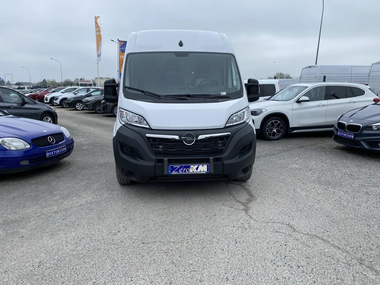 Vue frontale d'un fourgon Opel Movano blanc 2022 avec calandre noire et plaque "Zero KM" sur un parking.