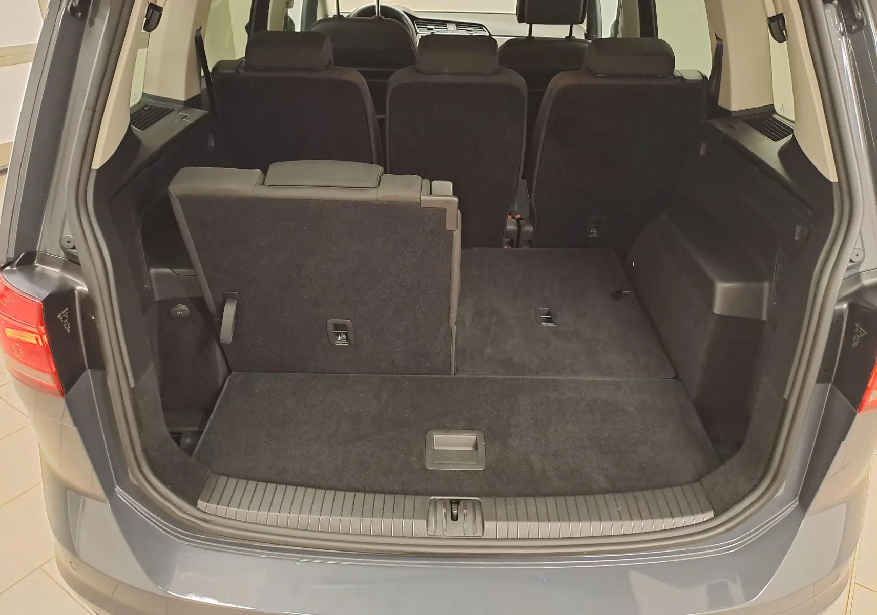 Vue arrière du coffre ouvert d’un Volkswagen Touran gris Dauphin 2024, sièges arrière partiellement rabattus.