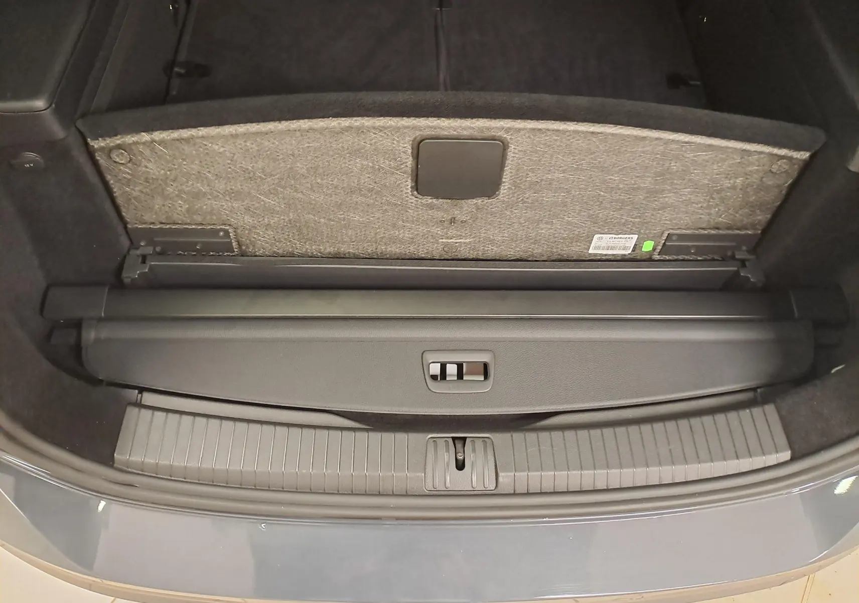 Vue rapprochée du coffre ouvert d’un Volkswagen Touran gris Dauphin 2024, avec cache-bagages et plancher relevé.