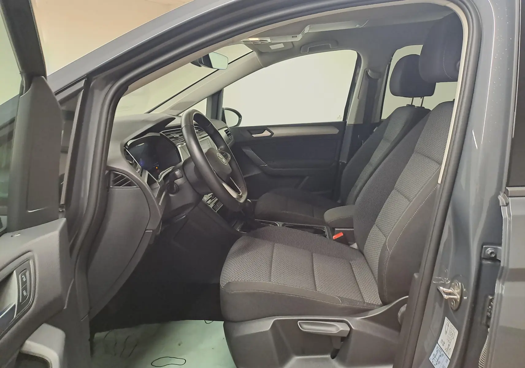 Vue intérieure côté conducteur du Volkswagen Touran gris Dauphin 2024, sièges tissu et tableau de bord moderne.