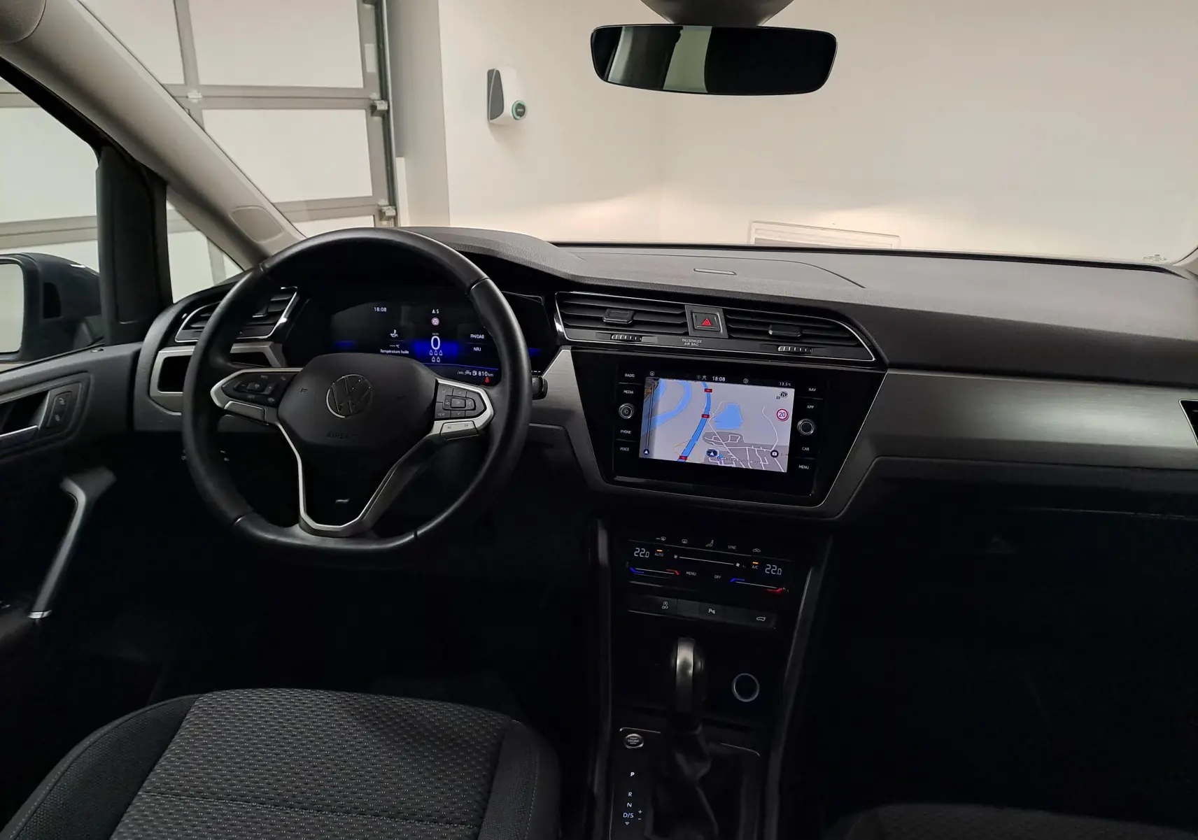 Vue intérieure avant du Volkswagen Touran 2024, tableau de bord noir avec écran tactile et volant multifonction.