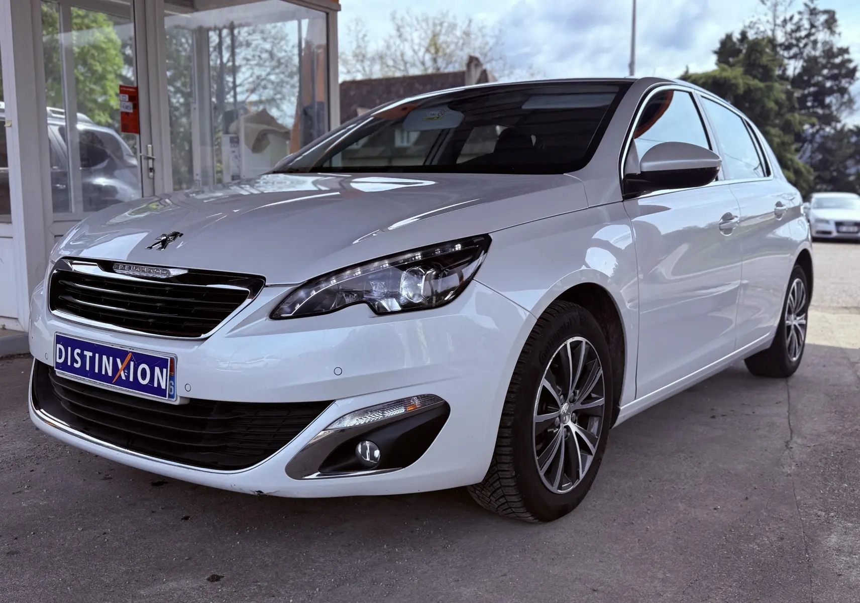 Peugeot 308 blanc nacré vue 3/4 avant droit, avec jantes alliage et calandre noire brillante.