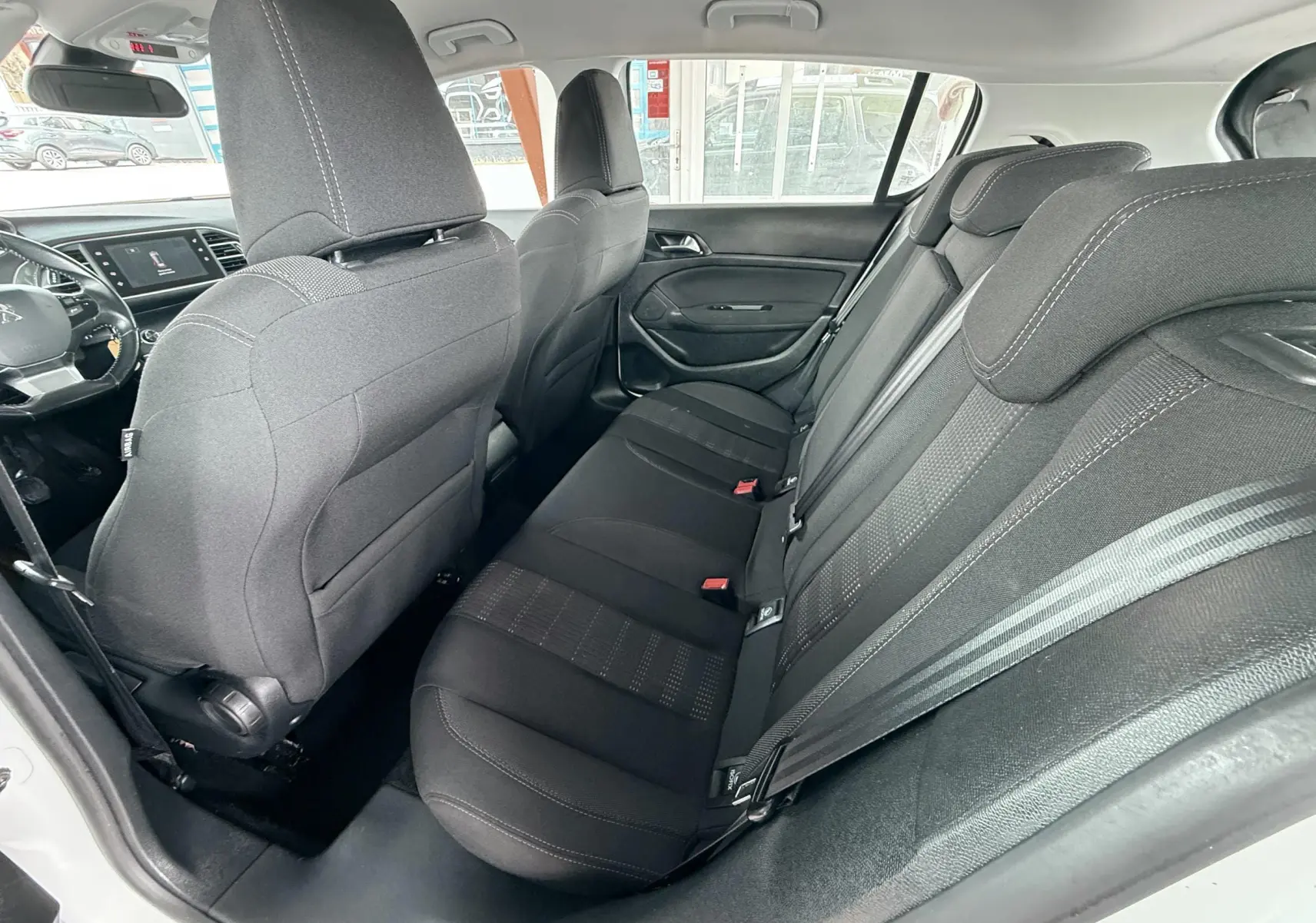 Vue intérieure arrière droite de la Peugeot 308 blanche, montrant les sièges arrière en tissu noir et les appuie-têtes.