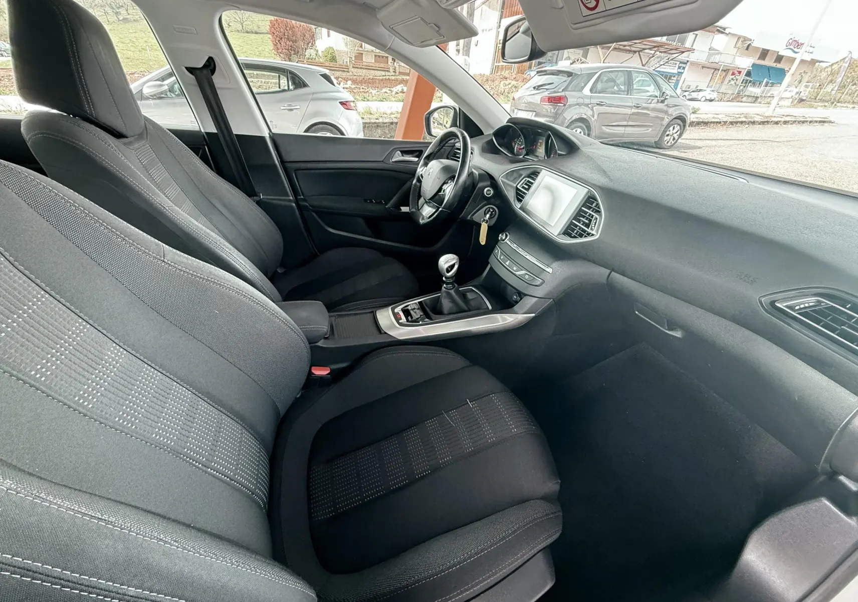 Intérieur noir de la Peugeot 308 2016, vue côté passager avant avec tableau de bord et levier de vitesse manuel visibles.