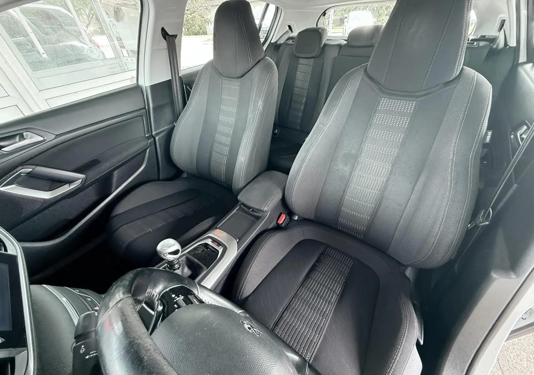 Vue intérieure avant droite de la Peugeot 308 avec sièges tissu noir et levier de vitesse manuel visible.