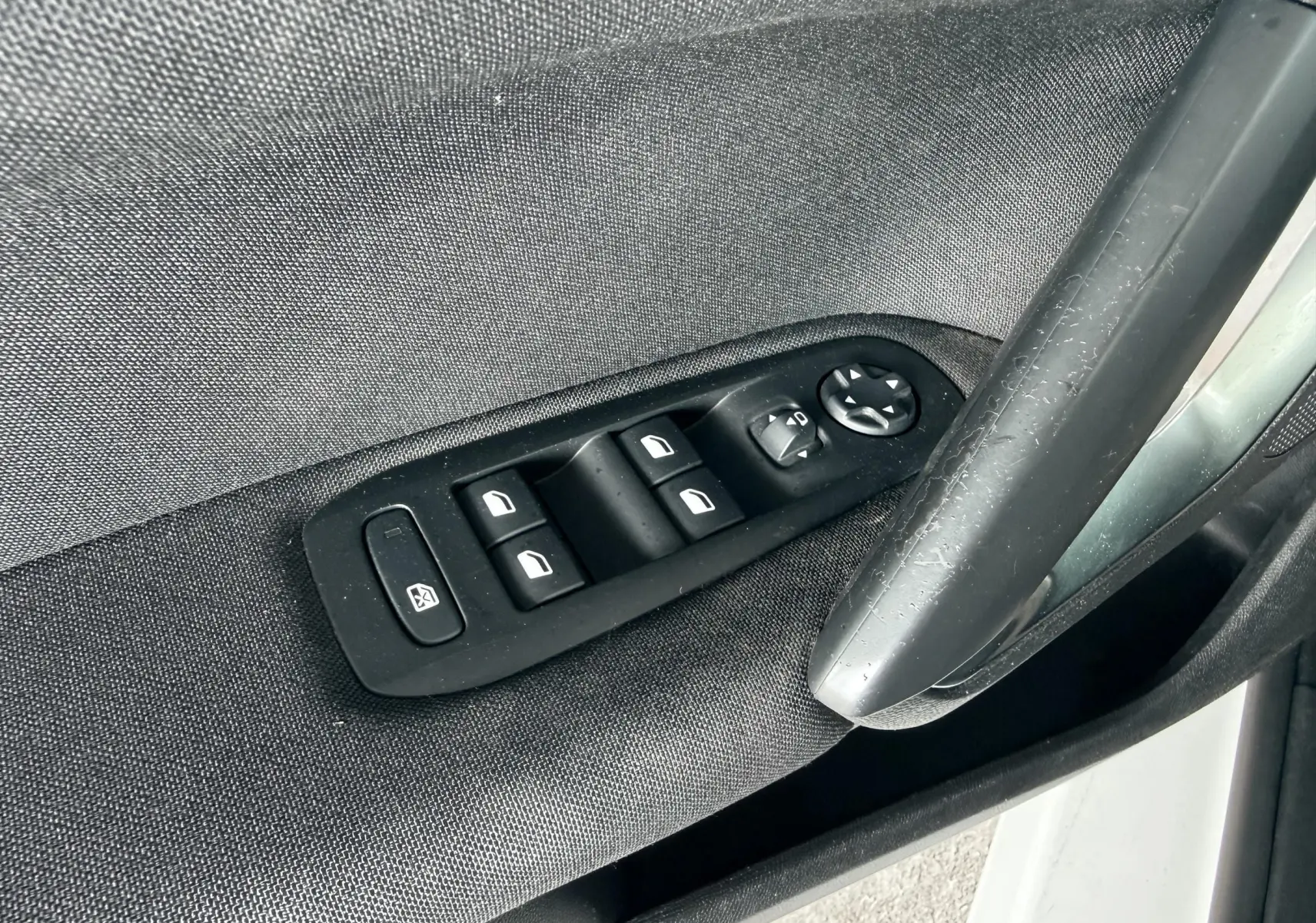 Gros plan sur les commandes de lève-vitres et rétroviseurs côté conducteur d’une Peugeot 308 blanche nacrée.