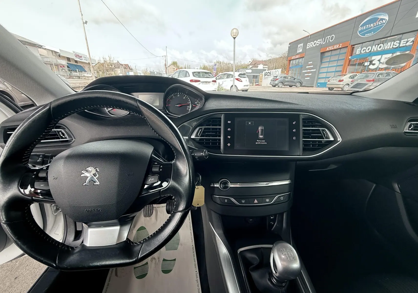 Vue intérieure du tableau de bord noir et volant Peugeot 308, avec écran tactile et levier de vitesses manuel visible.