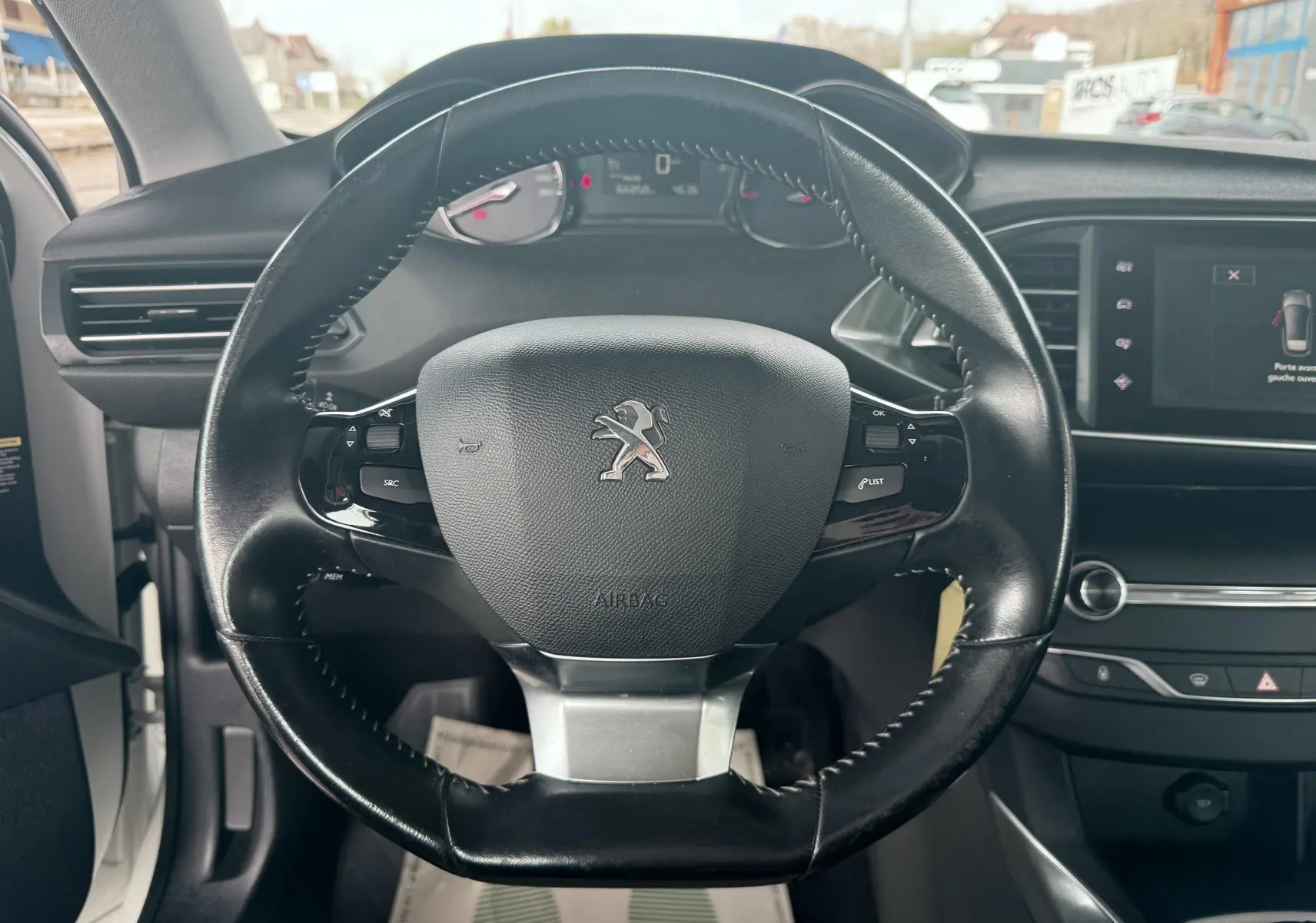Vue centrée sur le volant noir de la Peugeot 308 2016, avec tableau de bord et écran tactile visibles à droite.