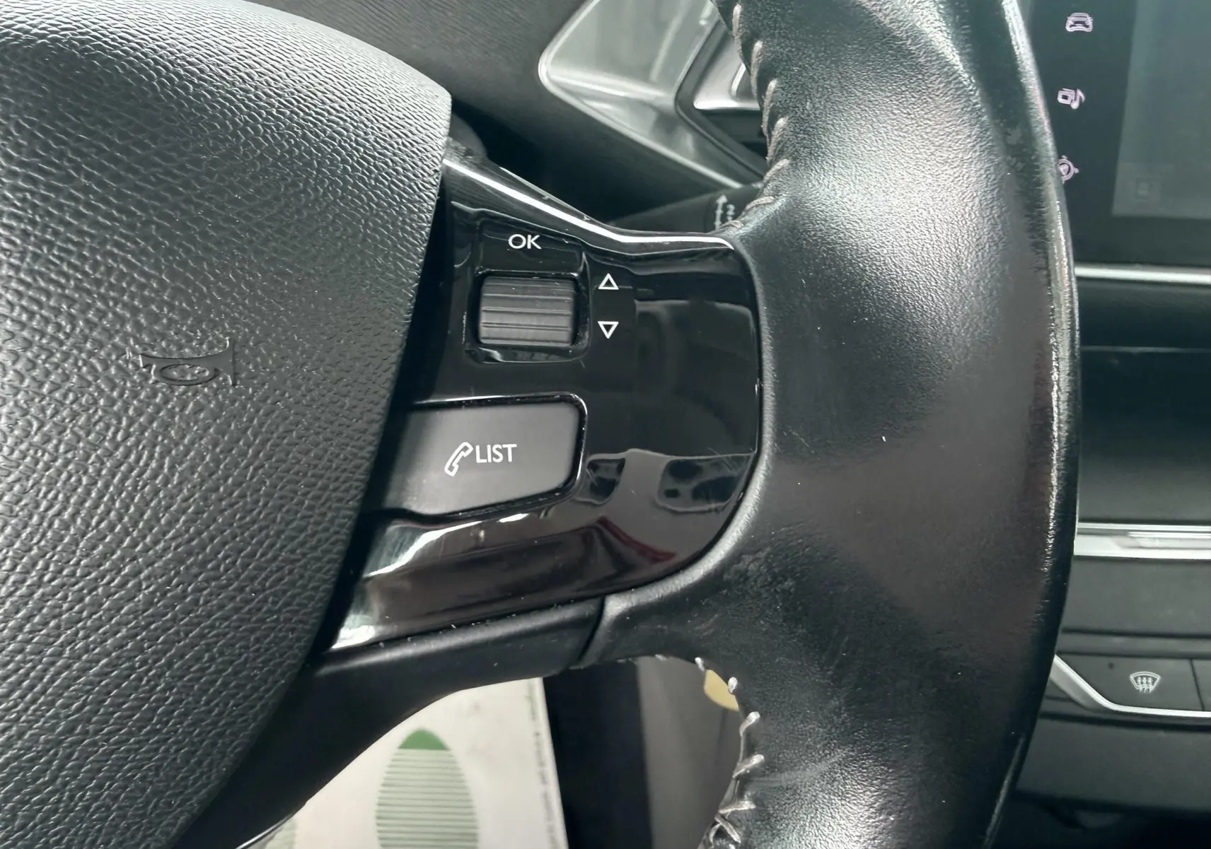 Gros plan sur le volant noir de la Peugeot 308 2016 avec commandes intégrées et finition brillante.