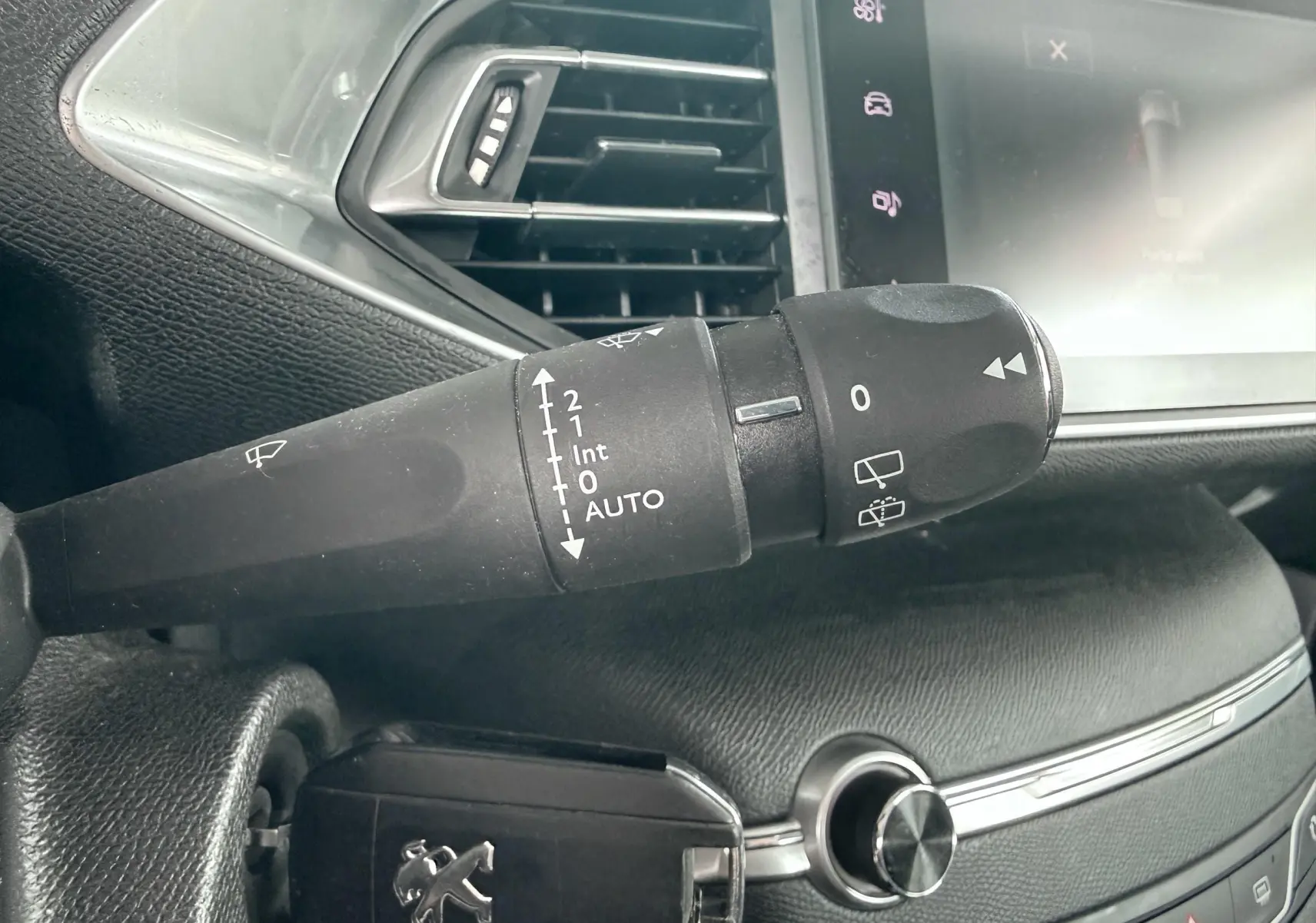Gros plan sur la commande d’essuie-glace et la clé Peugeot dans l’habitacle noir de la 308 blanche.