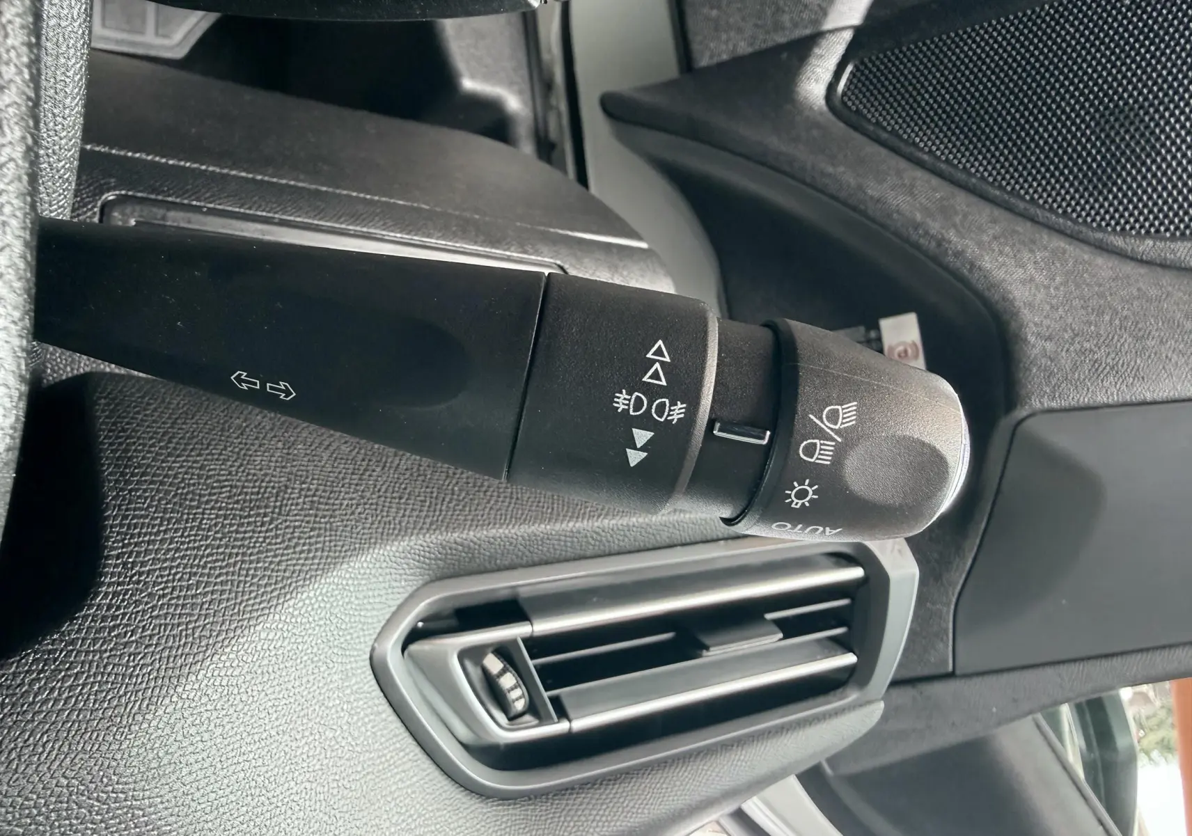 Gros plan sur la commande des phares et clignotants côté gauche du tableau de bord noir d'une Peugeot 308 blanche.