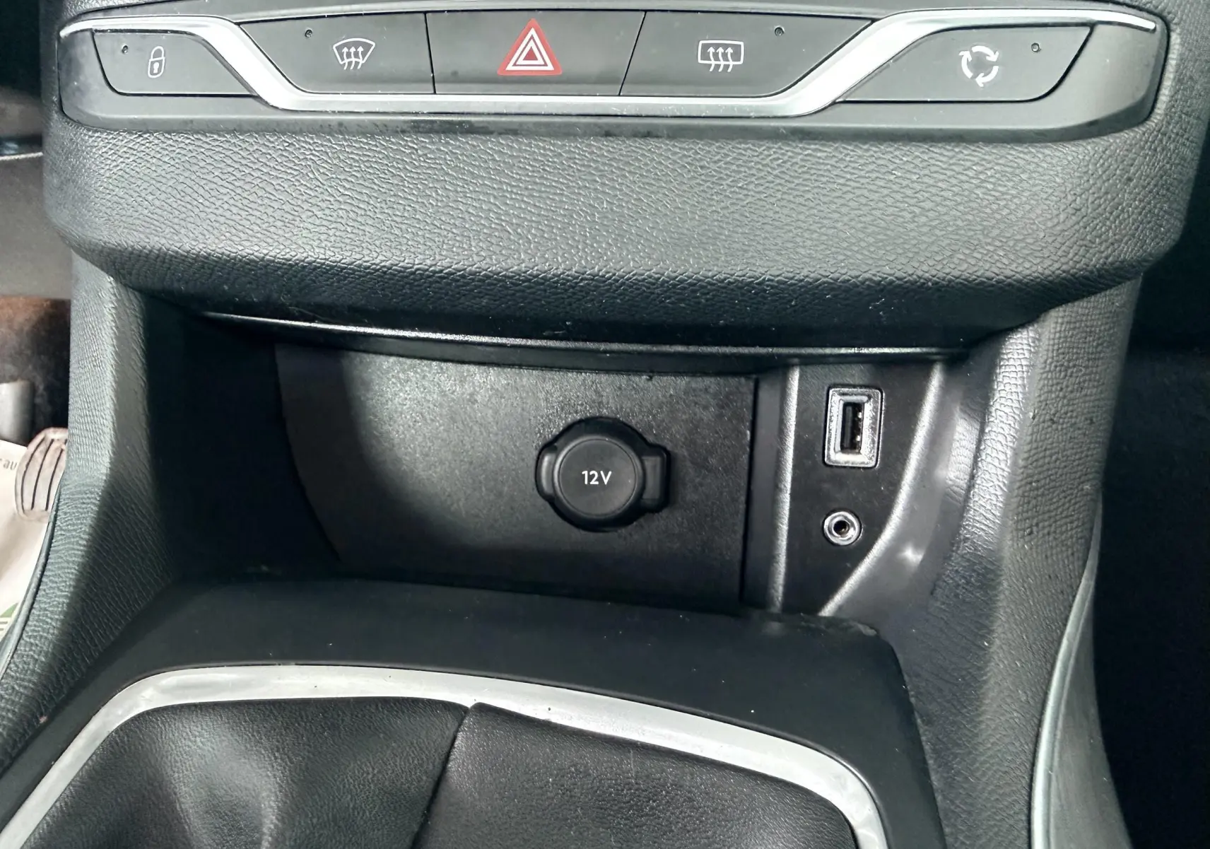 Vue rapprochée de la console centrale noire d’une Peugeot 308 avec prise 12V, port USB et boutons de commande.