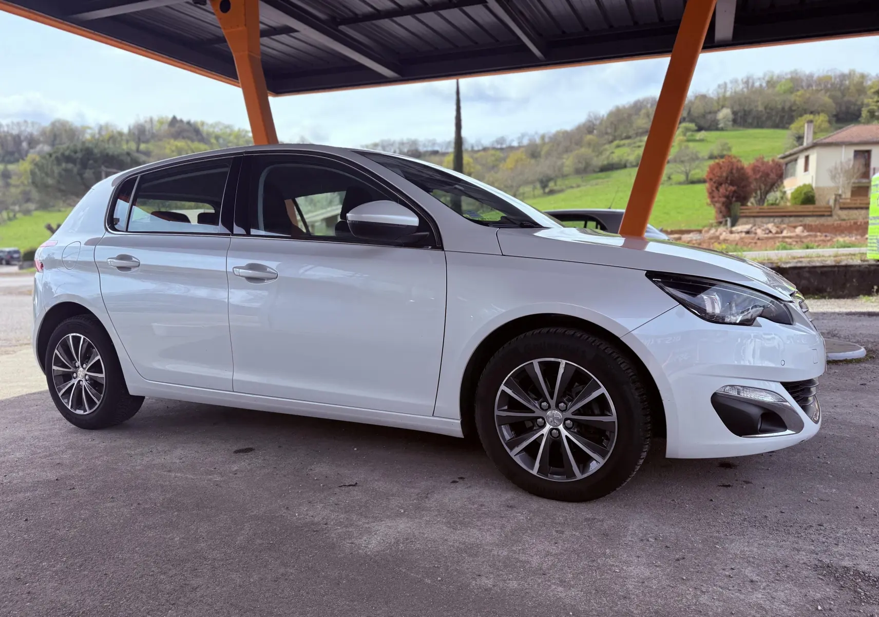 Vue latérale droite d'une Peugeot 308 blanche nacrée 5 portes sous abri avec jantes alliage et rétroviseurs blancs.