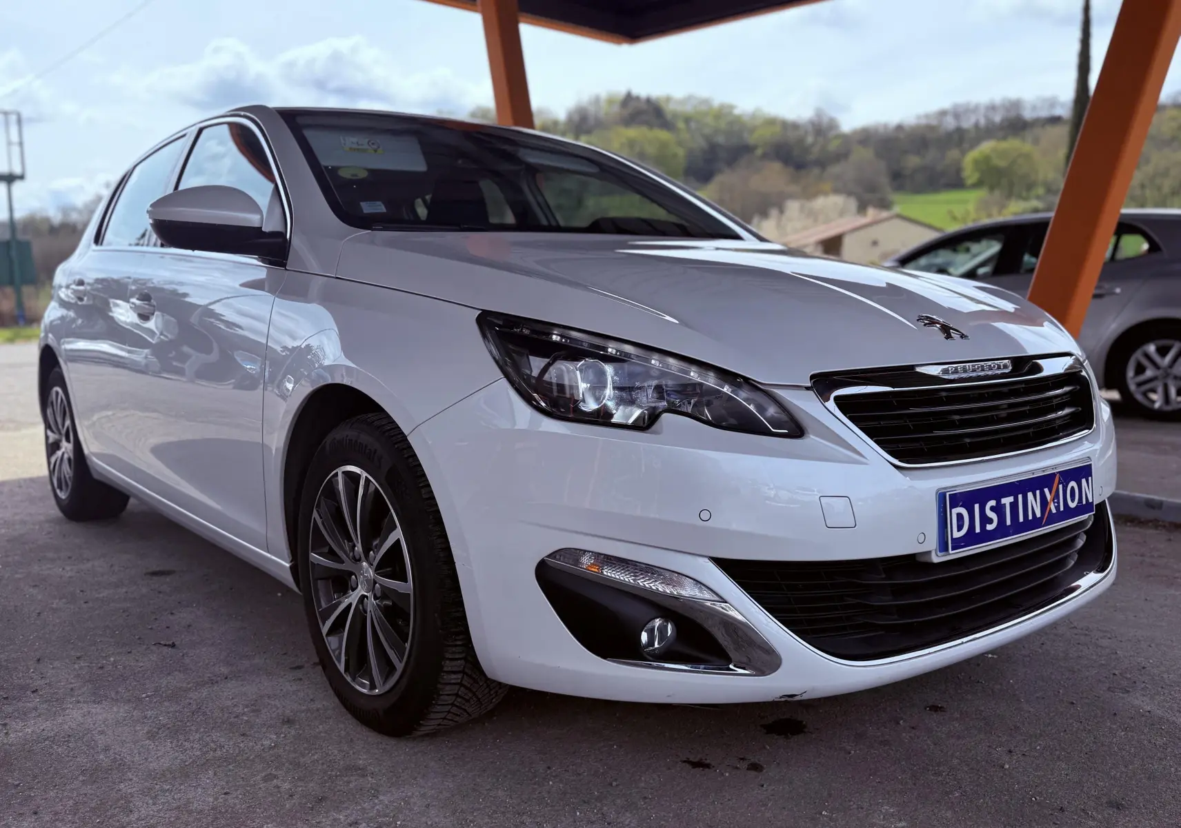 Peugeot 308 blanche vue en 3/4 avant droit sous abri avec jantes alliage et plaque Distinxion.