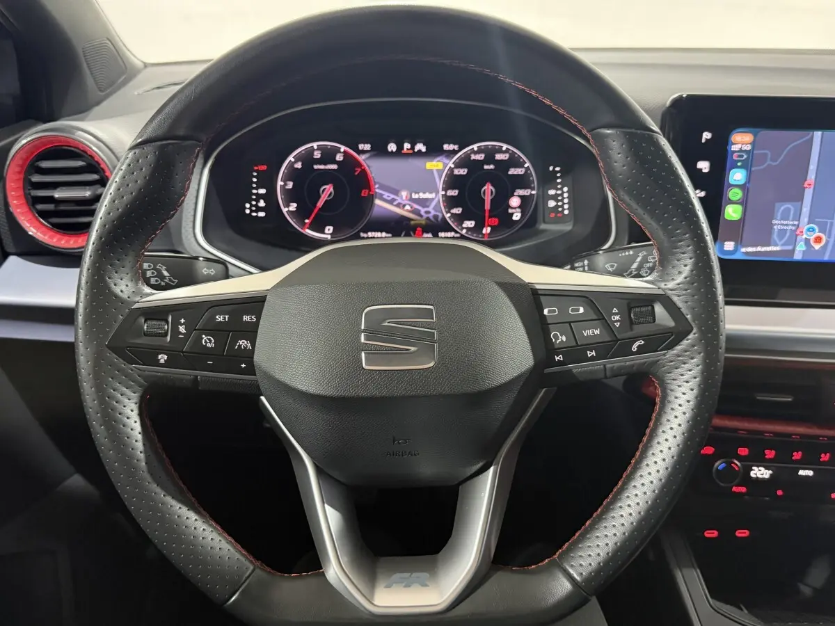 Vue rapprochée du volant cuir perforé noir avec surpiqûres rouges et tableau de bord digital de la SEAT Ibiza 2024 gris foncé.