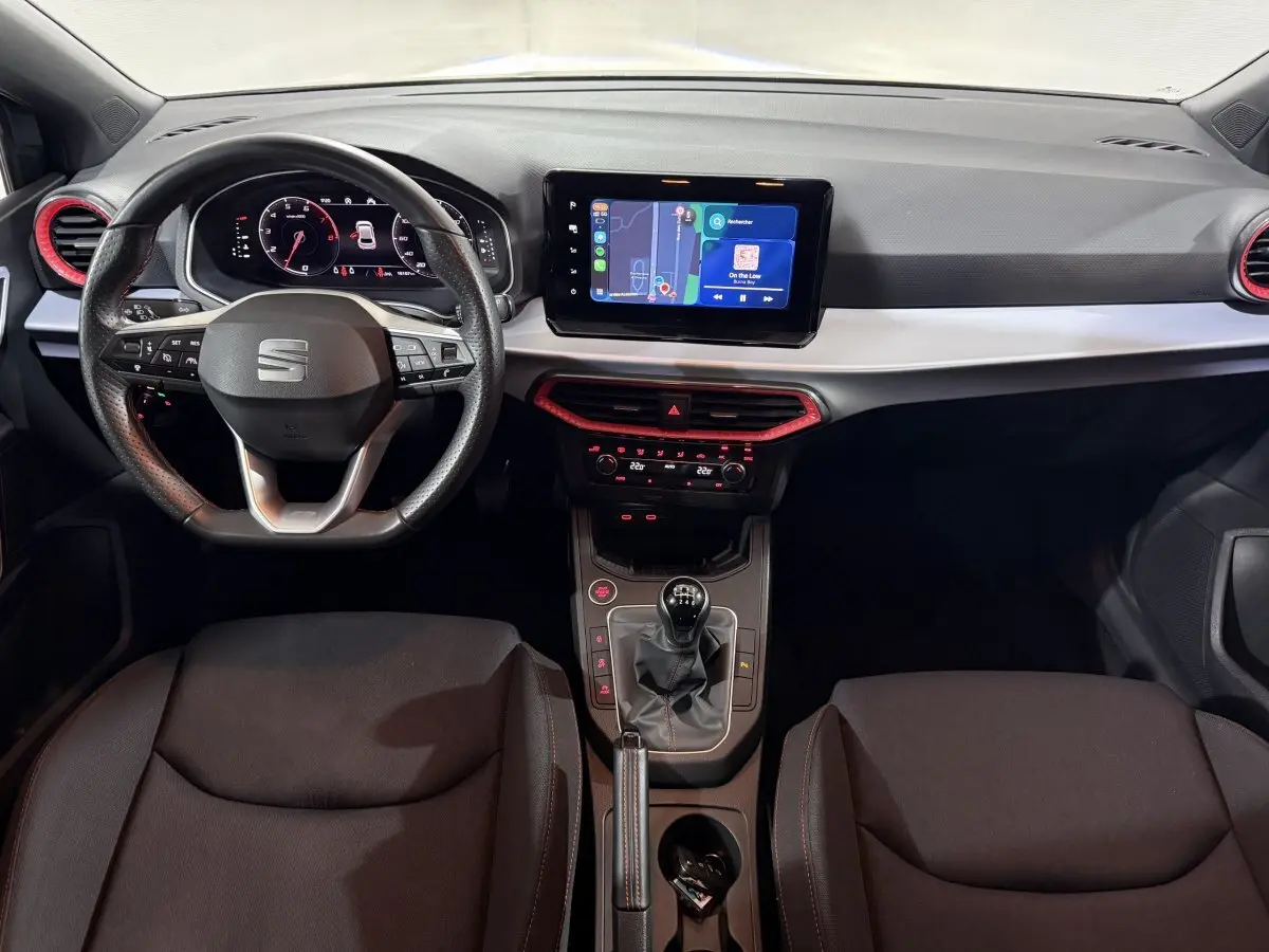 Vue intérieure frontale du tableau de bord de la SEAT Ibiza 1.0 TSI 110 FR avec volant cuir, écran tactile et détails rouges.