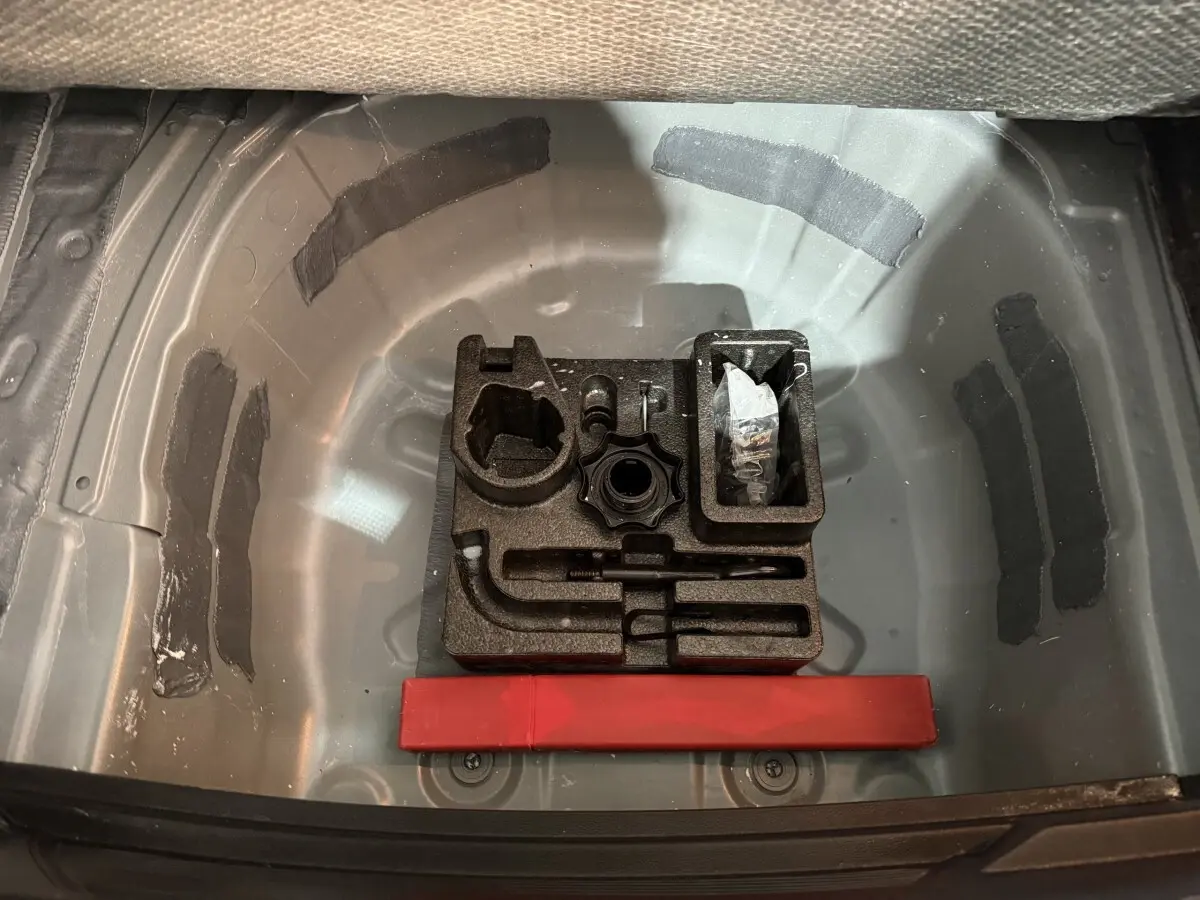 Vue plongeante sur le coffre ouvert d'une SEAT Ibiza gris foncé, montrant le rangement outils et espace pour roue de secours.