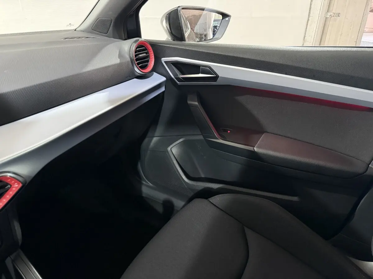 Intérieur côté passager de la SEAT Ibiza 2024 gris foncé, avec aérateurs rouges et garnitures argentées.