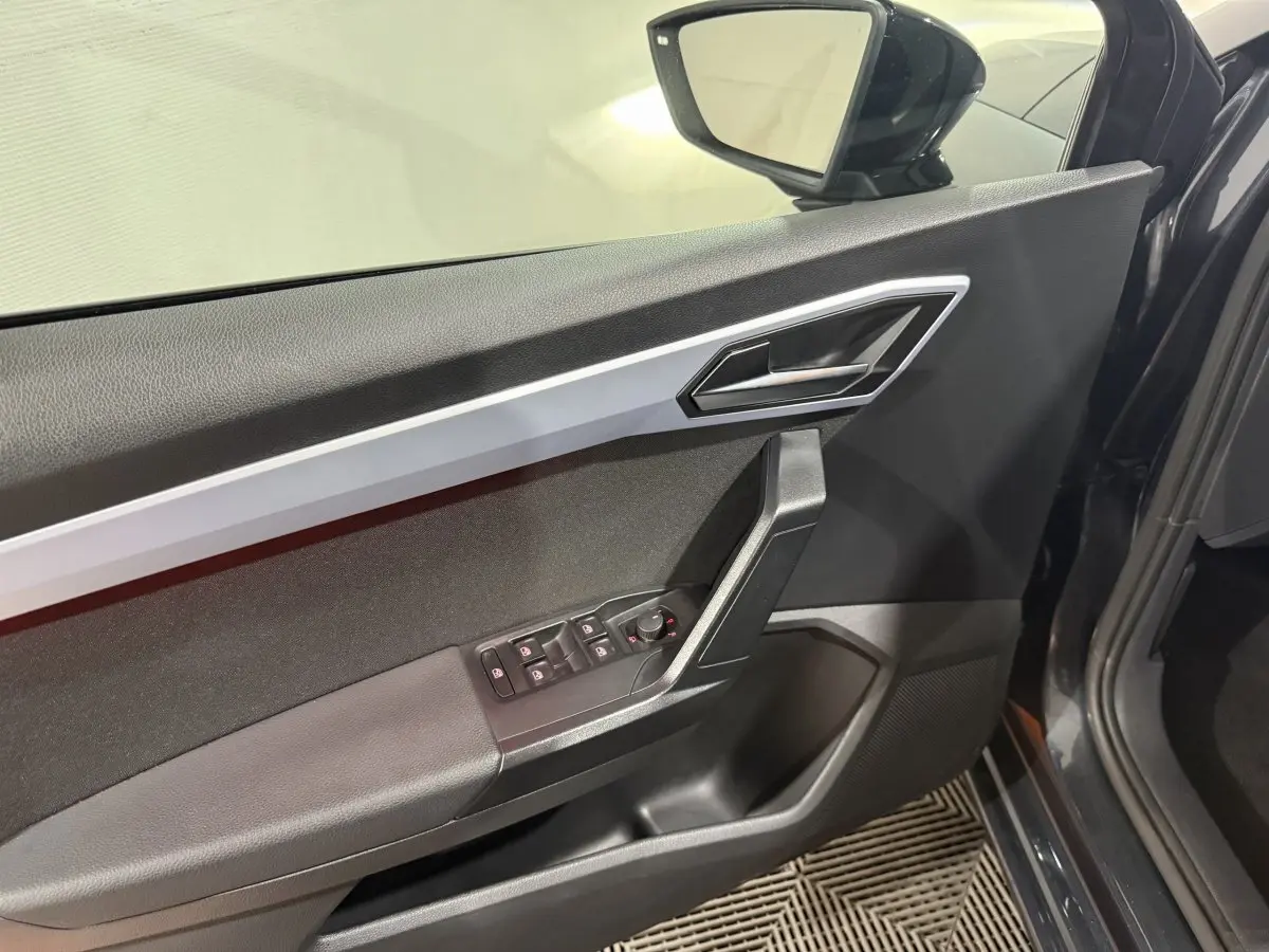Vue intérieure côté gauche de la porte avant gris foncé de la SEAT Ibiza 1.0 TSI 110 FR avec commandes électriques et poignée argentée.