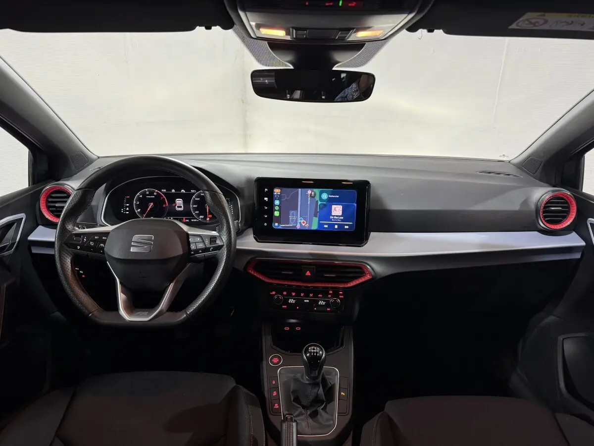 Vue intérieure avant de la SEAT IBIZA 1.0 TSI 110 FR 2024, tableau de bord noir avec touches rouges et écran tactile central.