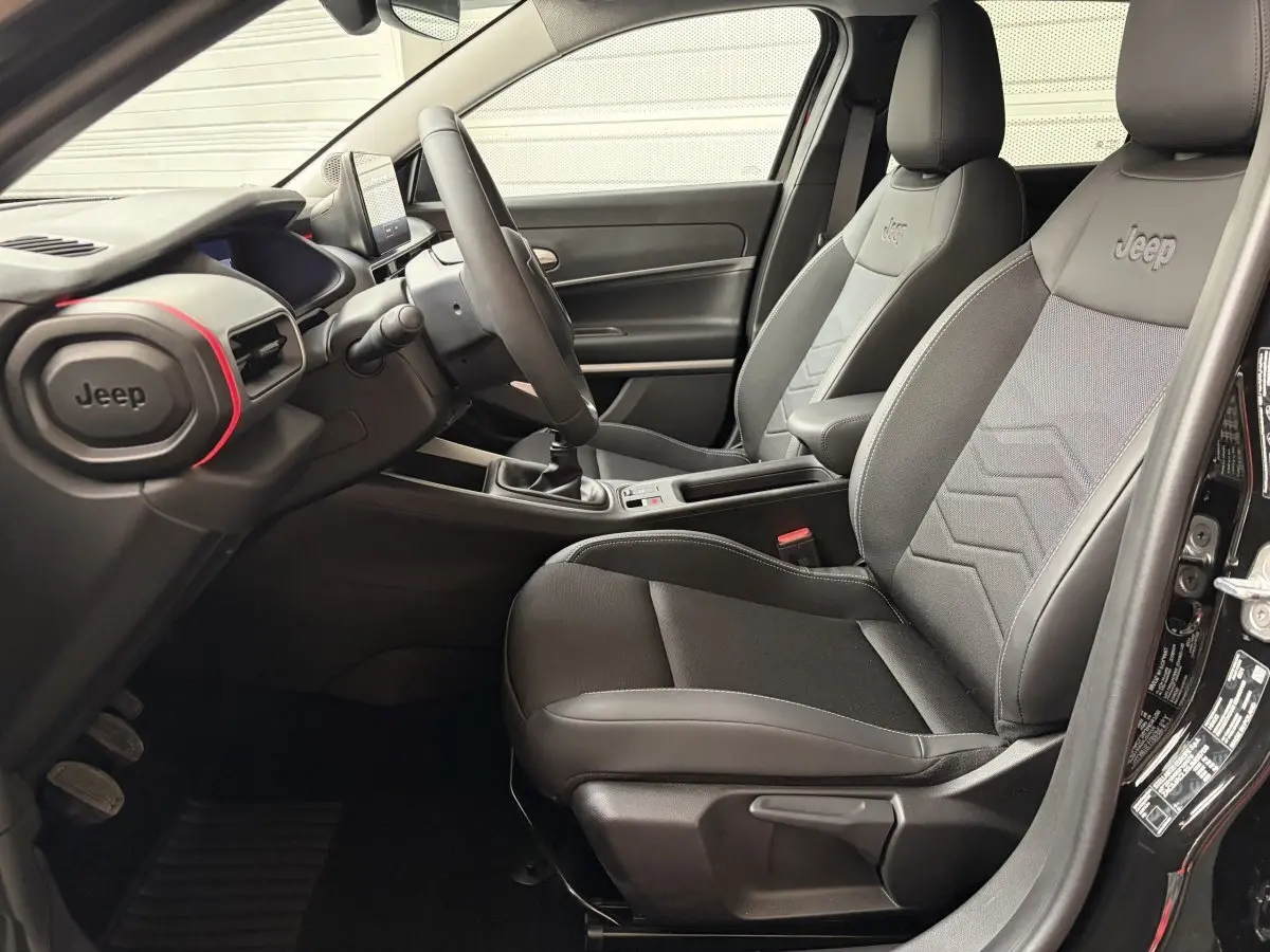 Vue intérieure côté conducteur du Jeep Avenger 2025 noir, sièges tissu avec logo Jeep brodé et volant multifonctions.