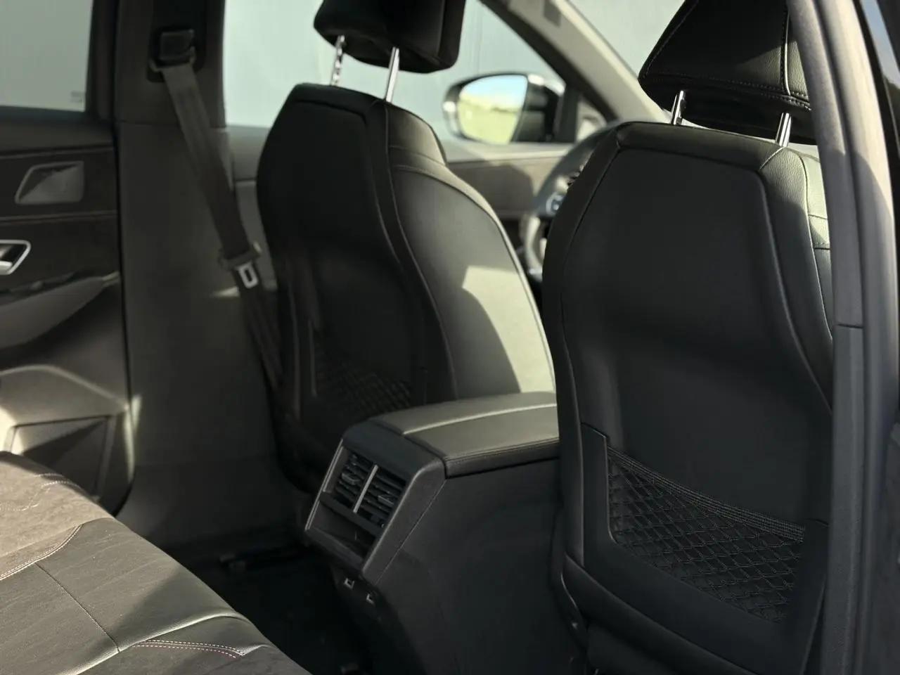 Vue arrière intérieure du DS7 2025 noir Perla montrant les sièges avant en cuir et la console centrale avec aérateurs arrière.