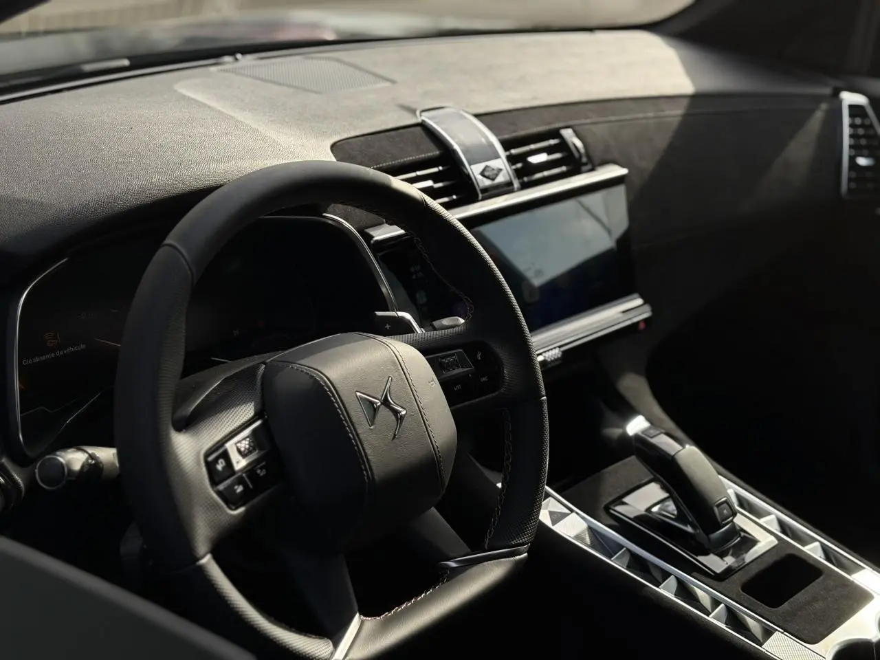 Intérieur du DS7 2025 vu côté conducteur, volant cuir noir avec surpiqûres, console centrale et écran tactile visibles.