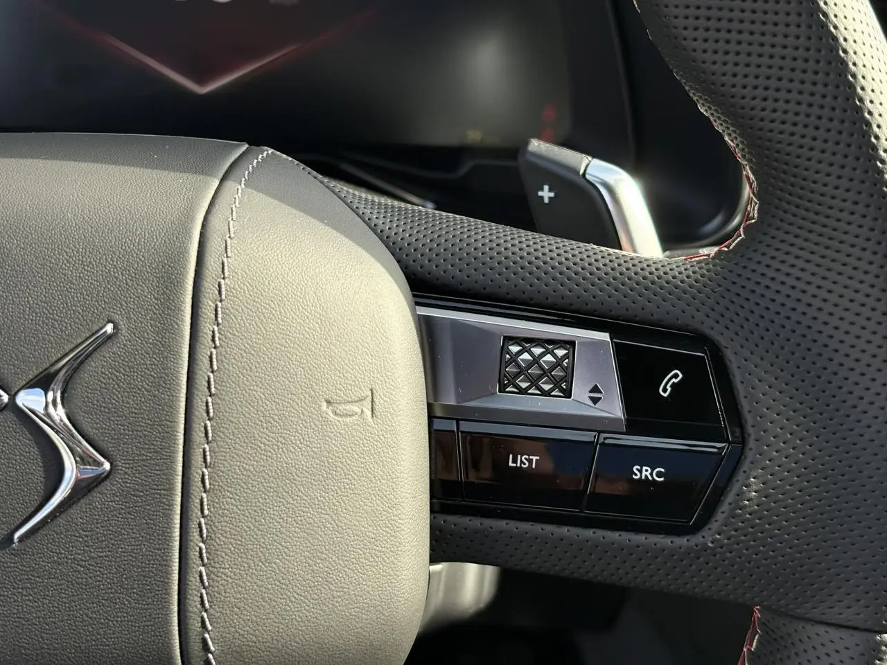 Gros plan sur le volant en cuir perforé noir avec surpiqûres rouges et commandes multifonctions du DS7 2025.