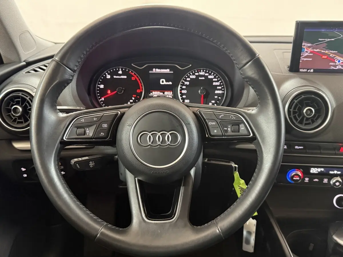Vue rapprochée du volant cuir noir d’une Audi A3 2.0 TDI 2018 avec tableau de bord et écran de navigation visible.