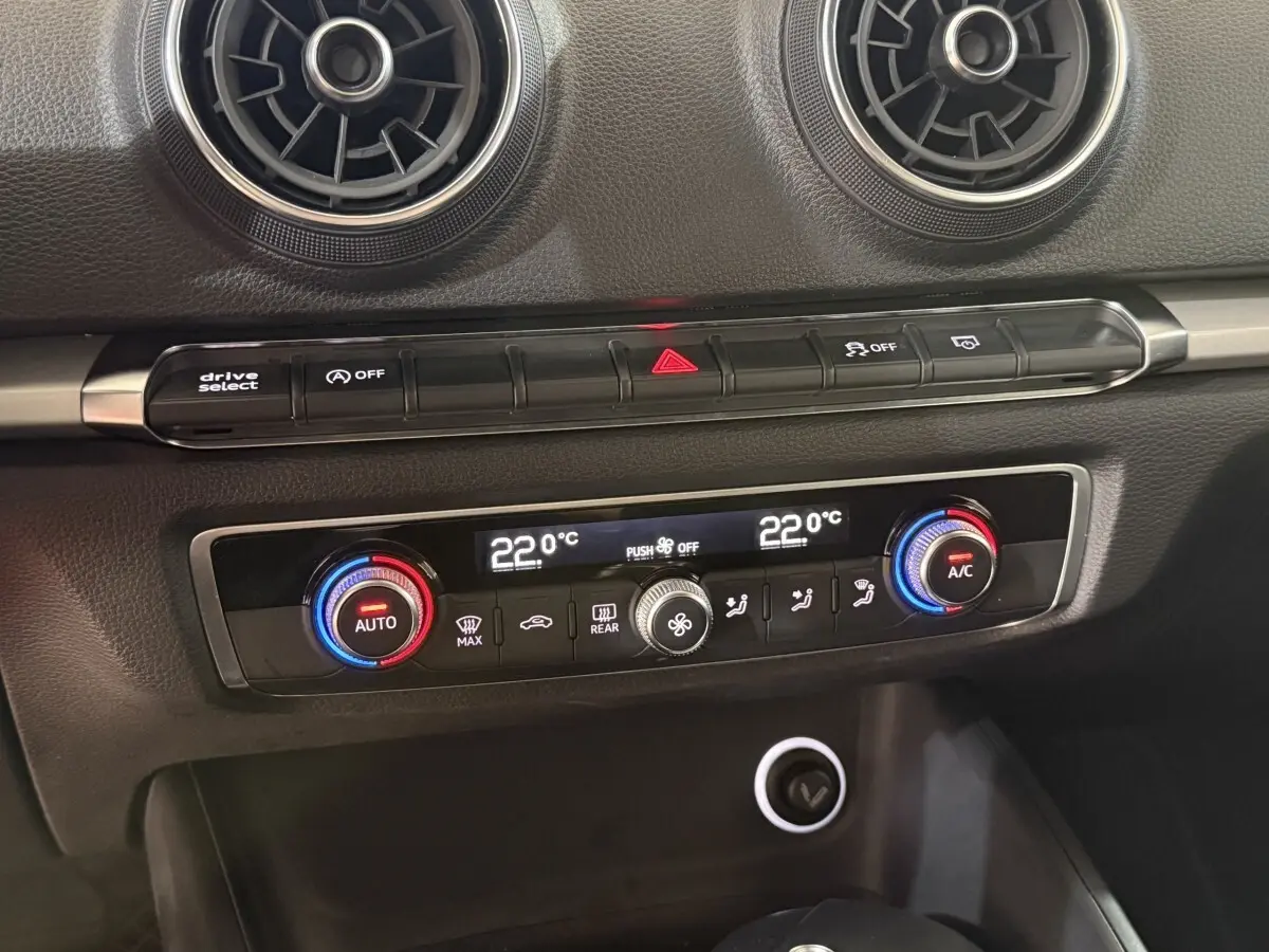 Détail de la console centrale de l'Audi A3 bleu, montrant la climatisation digitale bi-zone et les aérateurs ronds noirs.