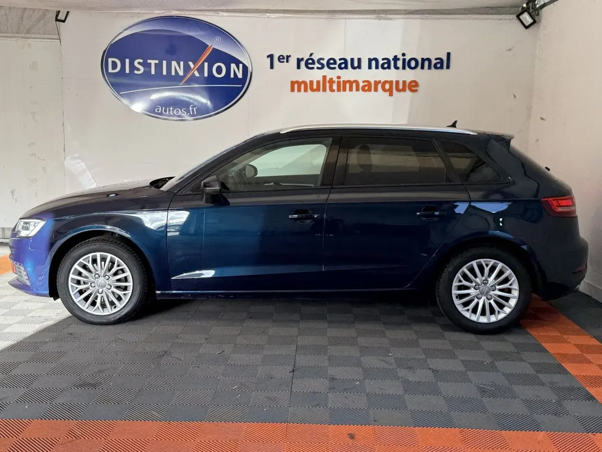 Profil côté gauche d'une Audi A3 2.0 TDI Business Line bleu foncé, avec jantes alliage et vitres teintées, en intérieur showroom.