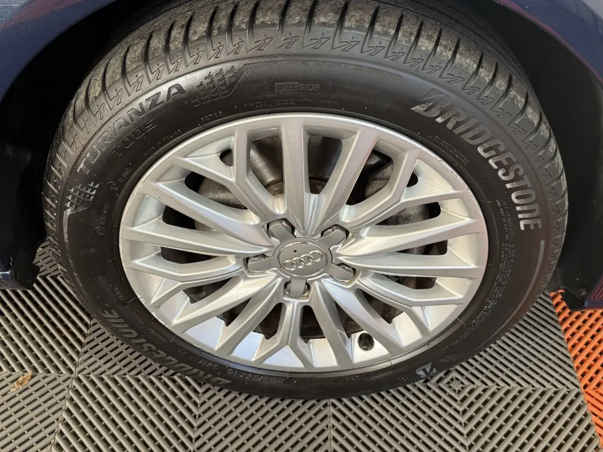 Gros plan sur la roue avant gauche d'une Audi A3 bleu, jante alliage argentée avec logo Audi au centre.