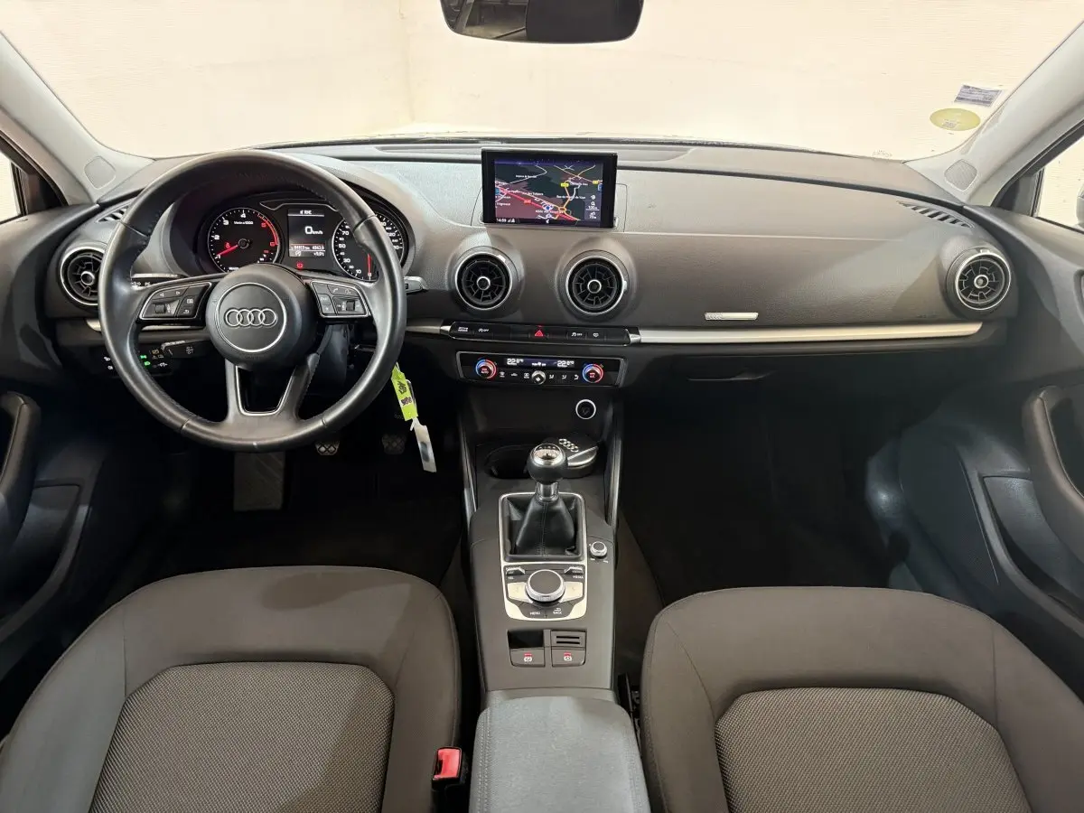 Vue intérieure frontale de l'Audi A3 2018 avec tableau de bord noir, volant cuir multifonctions et écran central navigation.