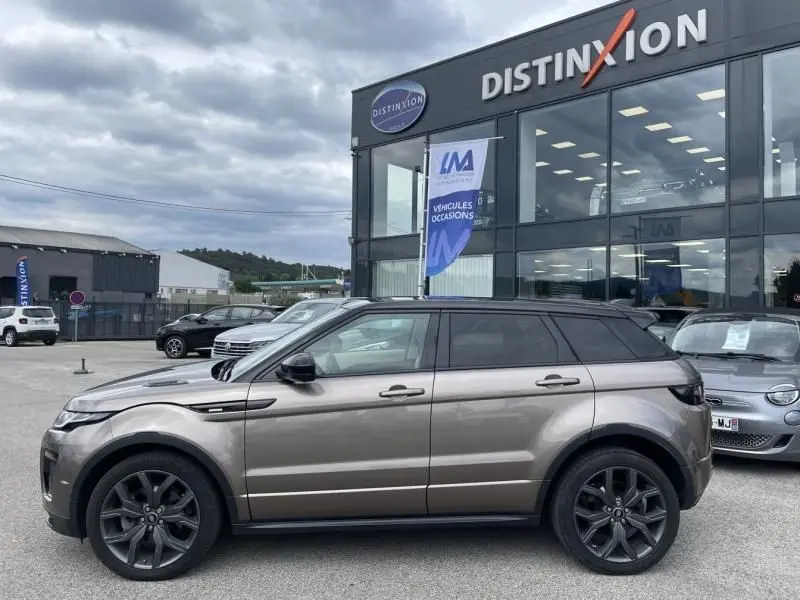 Vue latérale droite d'un Range Rover Evoque TD4 180 Autobiography marron métal 2017 avec toit noir devant un concessionnaire.