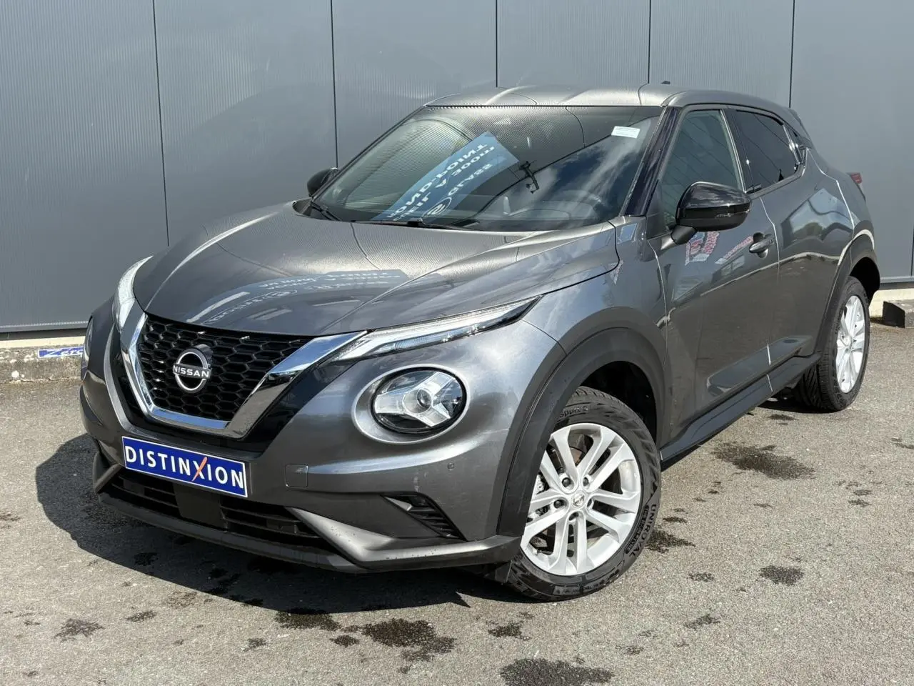 Nissan Juke gris Dark Metal en 3/4 avant droit, avec jantes alliage blanches et calandre chromée distinctive.
