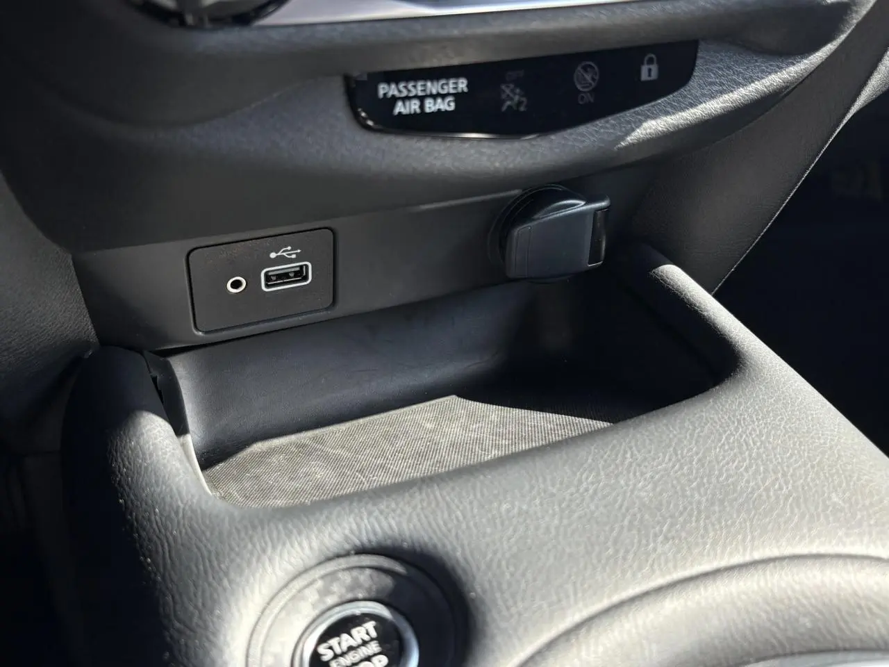Gros plan sur la console centrale noire du Nissan Juke 2024 avec prise USB, prise 12V et bouton Start/Stop visible.