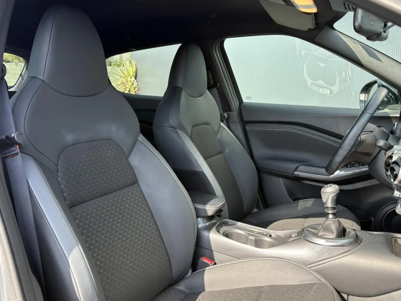 Vue intérieure côté droit du Nissan Juke 2024, sièges avant en sellerie mixte noir et gris avec levier de vitesses manuel.