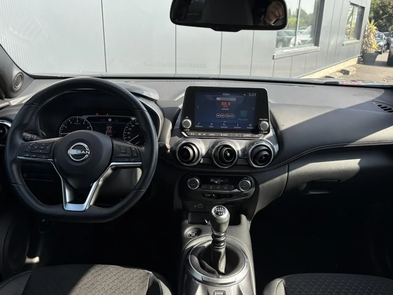 Vue intérieure du tableau de bord du Nissan Juke 2024 avec volant multifonction, écran tactile et levier de vitesses manuel.