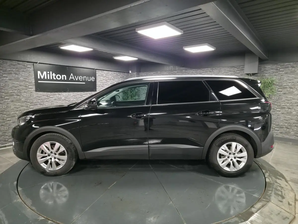 Profil côté gauche d'un Peugeot 5008 noir métallisé 2021 dans un showroom avec jantes alliage 17 pouces.