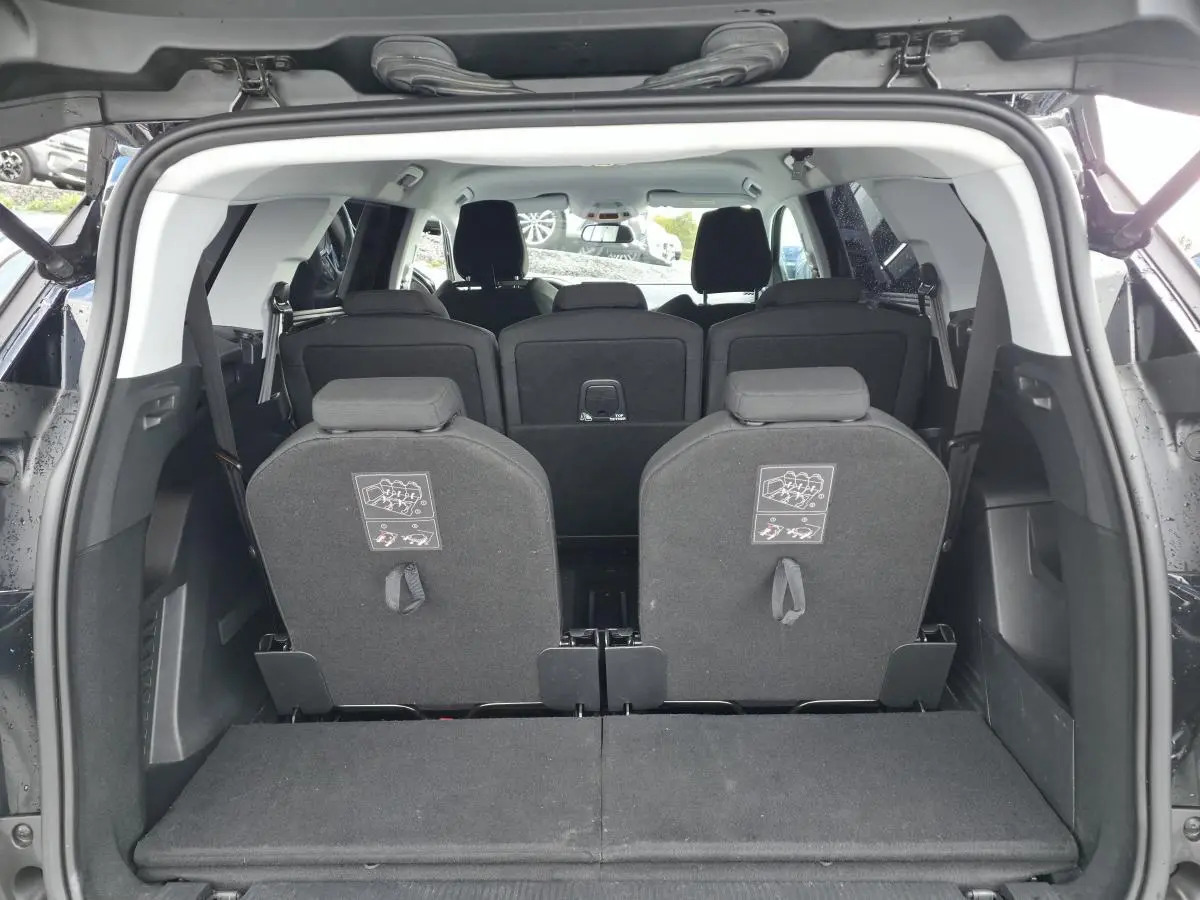 Vue arrière du coffre ouvert d'un Peugeot 5008 noir montrant les sièges escamotables du troisième rang relevés.