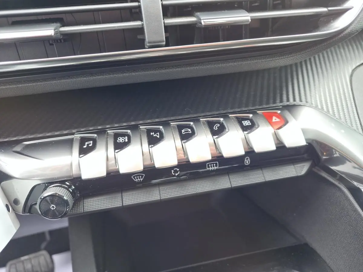 Gros plan sur la console centrale du Peugeot 5008 noir 2021, mettant en valeur les commandes chromées et le décor carbone.