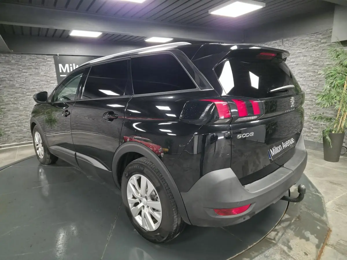 Vue 3/4 arrière droite du Peugeot 5008 noir avec attelage et jantes alliage dans un showroom intérieur.