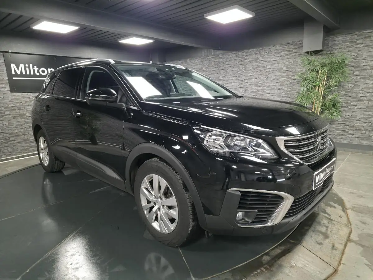 Peugeot 5008 noir vue 3/4 avant droit en intérieur avec calandre chromée et jantes alliage 17 pouces.