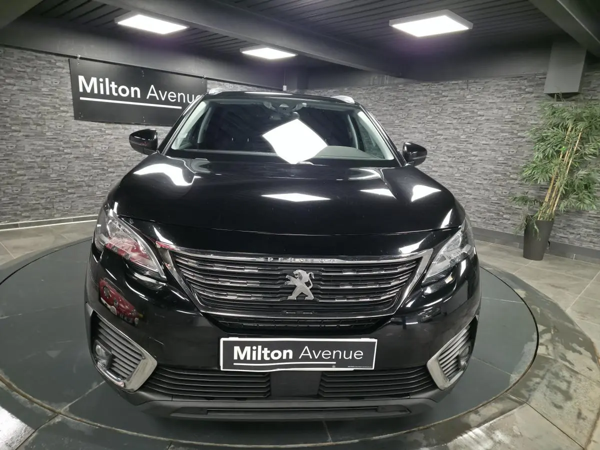 Vue frontale d'un Peugeot 5008 noir avec calandre chromée et feux LED, en intérieur sur plateau tournant.