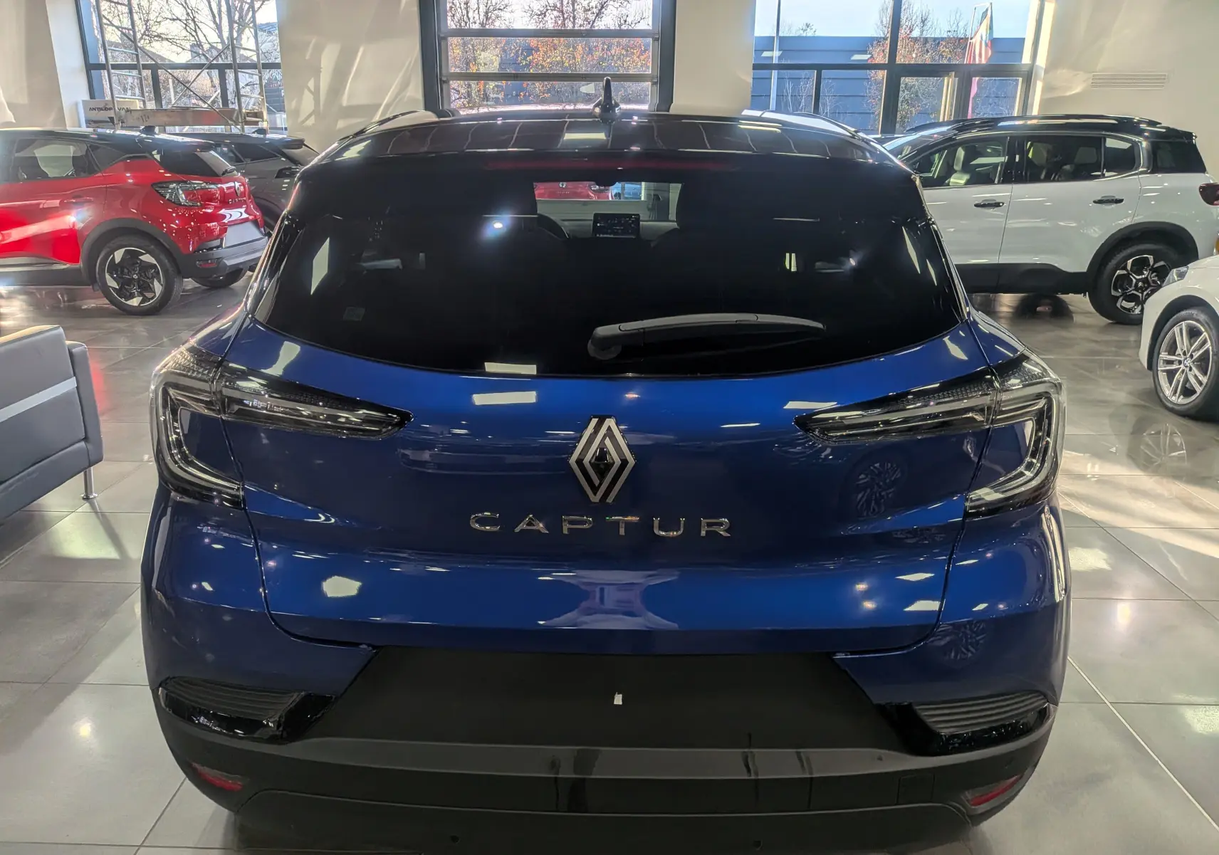 Vue arrière d'un Renault Captur 2025 bleu Iron avec toit noir dans un showroom lumineux.