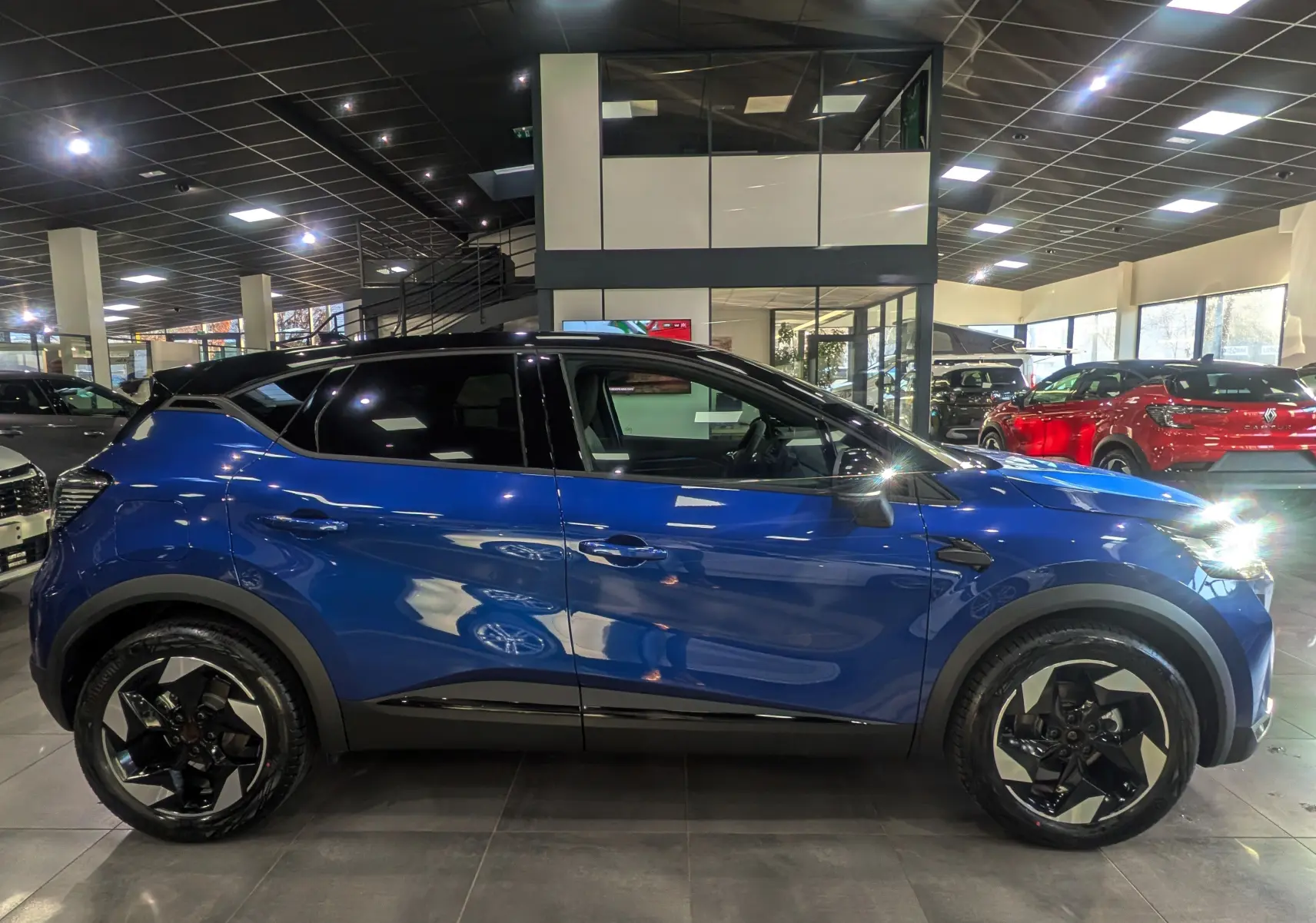 Vue latérale droite du Renault Captur 2025 bleu Iron avec toit noir, roues alliage 18 pouces en showroom.