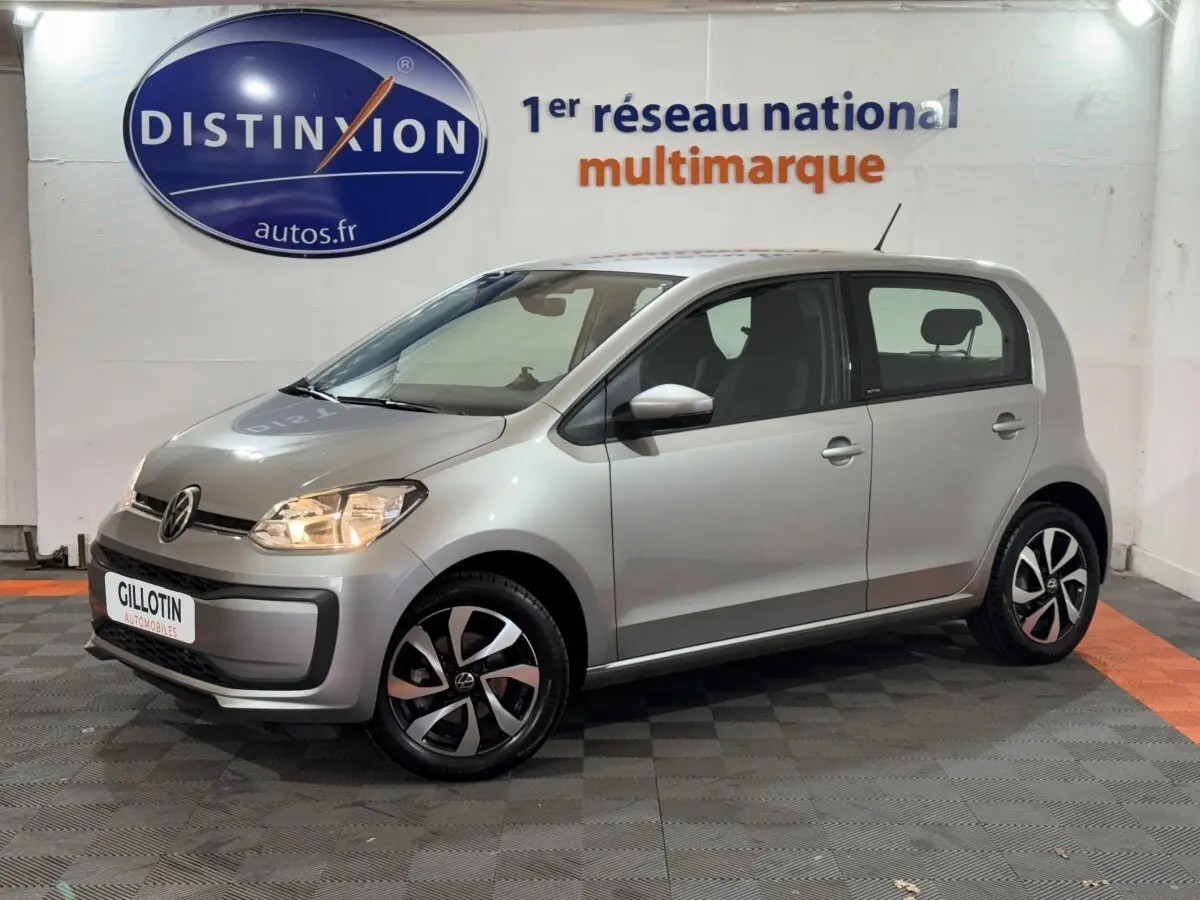 Volkswagen Up gris foncé vue 3/4 avant droit, phares allumés et jantes noires et argentées design moderne.