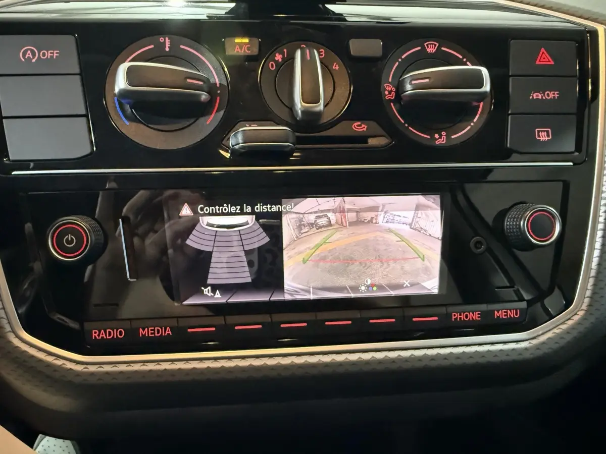 Vue rapprochée du tableau de bord de la Volkswagen Up 1.0 65 Active 2022, montrant l'écran de caméra de recul et les commandes de climatisation.